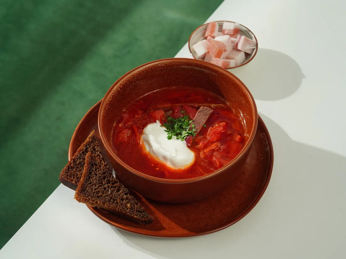 Красный борщ с говядиной, сметаной и зеленью, рядом ржаной хлеб
